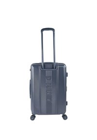 Maleta rígida de color gris oscuro con cuatro ruedas giratorias y asa telescópica extendida, recién colocada en posición vertical sobre un fondo blanco.