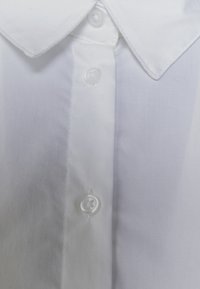 Camisa blanca de algodón de botones con un cuello clásico, botones transparentes y una textura suave, con una tapeta delantera bien cosida.