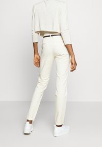 Jasnobeżowe spodnie o tapered fit, wykonane z miękkiej bawełny, z podwiniętymi mankietami, w połączeniu z białymi sneakersami. Prosty, minimalistyczny design.