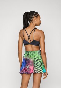 Soutien-gorge de sport noir avec des bretelles croisées, associé à une jupe colorée imprimée numériquement avec des motifs abstraits en vert, bleu et rose.