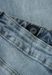 Tessuto in denim blu chiaro con cuciture visibili, dotato di una vita interna blu scuro e di un bottone metallico nero sulla parte superiore.