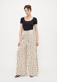 Black scoop neck top and beige wide-leg pants with a geometric black pattern. Fabric appears lightweight and flowy, suitable for warm weather.