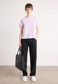 Camiseta de manga corta en color lila combinada con pantalones de pierna ancha negros. La modelo sostiene un bolso negro texturizado con un patrón de zigzag y lleva zapatillas blancas.