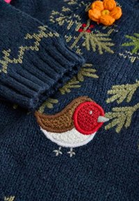 Navy gestrickter Pullover mit bunten gestickten Details, einschließlich eines Rotkehlchens, einer orangefarbenen Blume und grünen Blattakzenten. Gerippte Bündchen.