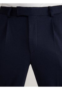 Dunkelblaue Anzughose mit glatter Oberfläche, vorn mit Falten und einem Gürtelloop ausgestattet, aus einem strukturierten Stoff gefertigt.