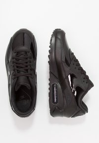 Svarta Nike Air Max-skor med slät lackläder och texturerade överdrag. Funktioner inkluderar en synlig luftkudde och gummitouch-sula.
