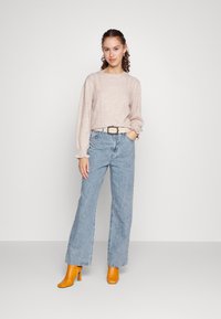 Beige teksturert genser med lange ermer, lyseblå høy midje jeans og oransje blokkhæl ankelstøvler. Beltet har et rundt sølvspenne.