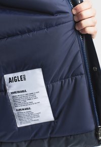 Námornícka puffer bunda zvnútra s prešívanou textúrou, zipsom a štítkom s pokynmi v angličtine a francúzštine.