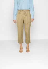 Calças cargo caqui com cintura ajustável, comprimento cropped e bolsos laterais, combinadas com uma camisa de mangas compridas azul claro e sandálias bege.