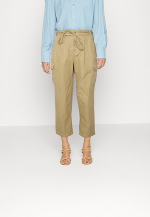 Calças cargo caqui com cintura ajustável, comprimento cropped e bolsos laterais, combinadas com uma camisa de mangas compridas azul claro e sandálias bege.