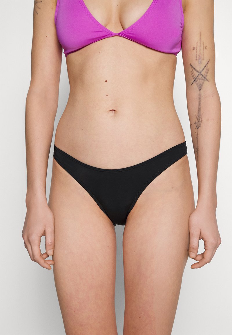 Juodas bikini apatinis trikotažas su žemu liemeniu, pagamintas iš lygaus medžiagos. Su minimaliais siūlais, patogiai sėdintis ant klubų.