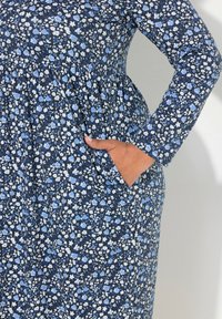 Kwiatowa sukienka uszyta z lekkiego materiału, z granatowym tłem oraz niebieskimi i białymi kwiatami. Długie rękawy i kieszenie po bokach.