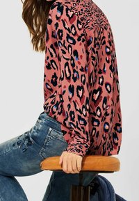 Blouse rose avec imprimé léopard noir et bleu, dotée de manches longues et d'une coupe décontractée, assortie à un jean en denim bleu.