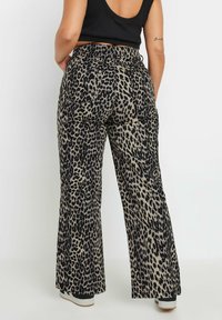 Pantalones acampanados de estampado de leopardo con fondo beige y manchas negras, con cintura alta y dos bolsillos traseros para un detalle adicional.