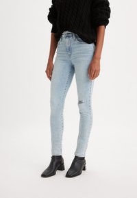 Világoskék, skinny farmernadrág, melynek térdén kopásos rész található. Denim anyagból készült, magas derekú, testhez simuló fazonú és finoman elhalványított. Fekete bokacsizma.