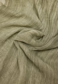 Lekki, przezroczysty materiał w stonowanej oliwkowej zieleni, z miękką, teksturowaną powierzchnią oraz subtelnymi różnicami w splotach i kolorze. Efekt zmarszczonego zwiewnego kroju.