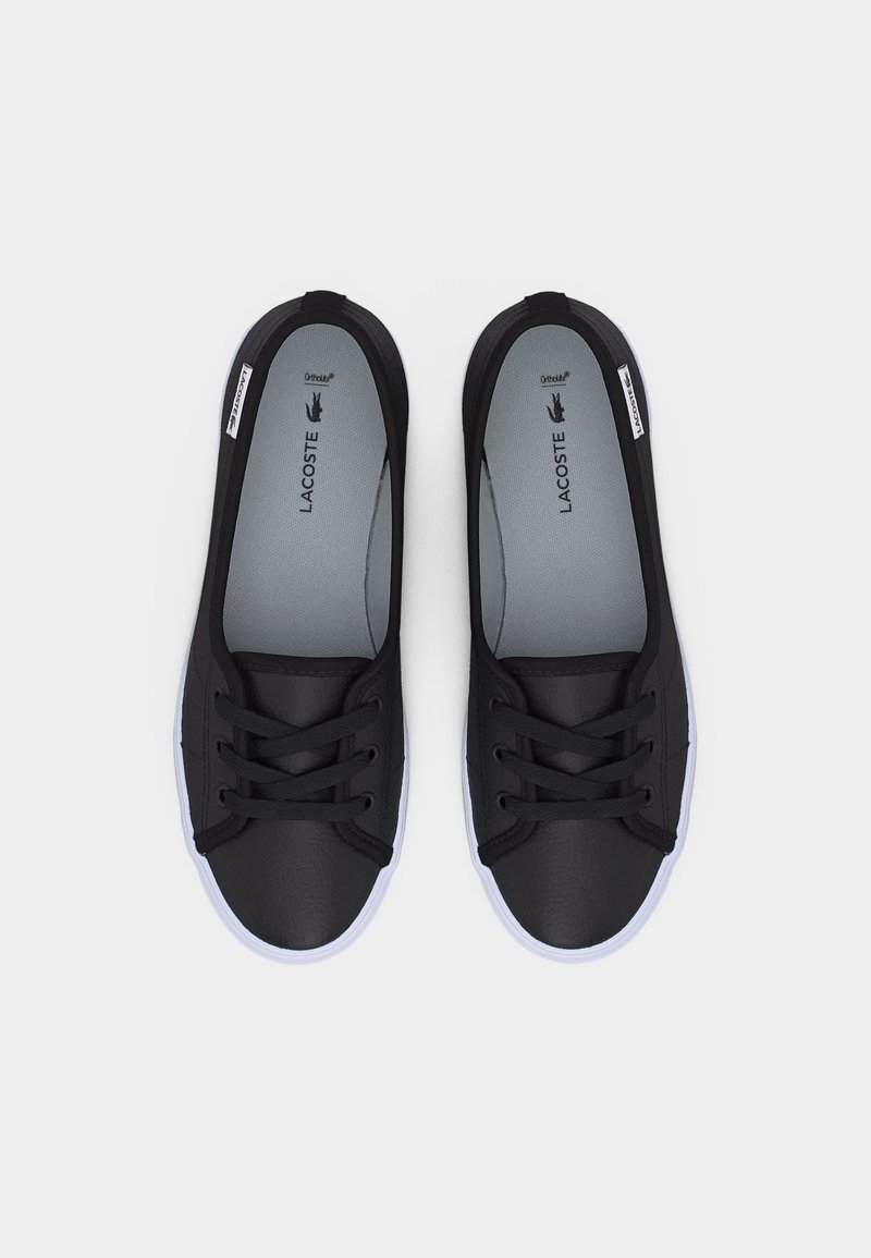 Paar schwarze Lacoste Freizeitschuhe mit Schnürsenkeln, weißen Sohlen, grauen Innensohlen und Markenetiketten auf hellgrauem Hintergrund.