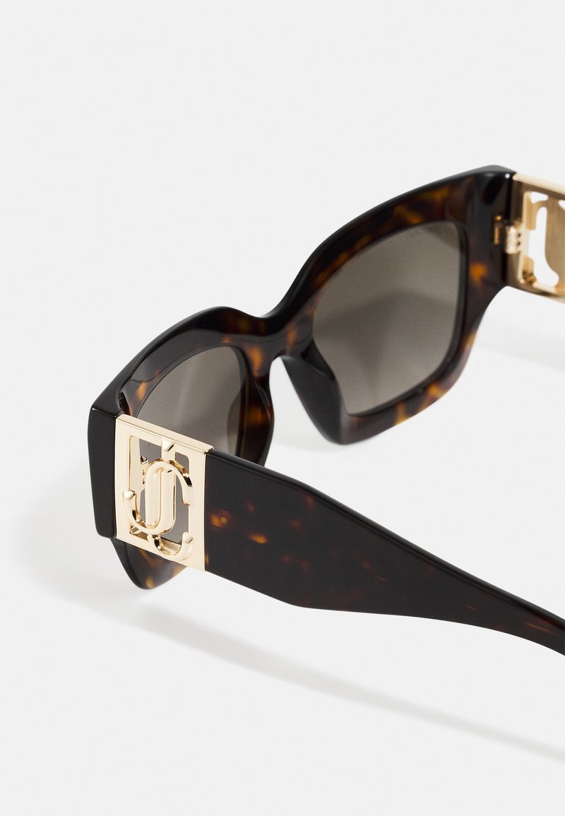 Lunettes de soleil écaille de tortue avec des verres foncés, dotées de garnitures en or sur les montures et d'un design carré avec une légère vague en haut.