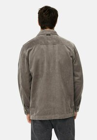 Grå ribfløjsjakke med krave, lange ærmer og lodret ribbet struktur. Har en let afslappet pasform og knaplukning.