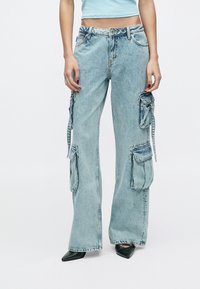 Világoskék farmer cargo nadrág széles szárakkal, több oldalzsebbel és laza szabással, kopott hatású és állítható részekkel.