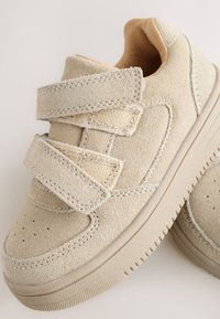 Beiget mokkanahkaiset tennarit, joissa on kaksi tarranauhaa, pyöreä kärki, kuvioitu kumipohja ja ommellut yksityiskohdat.