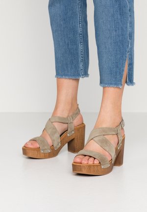 Szare sandały na wysokim obcasie z zamszu, z krzyżującymi się paskami i drewnianą platformą. Charakterystyczne elementy to srebrne ozdoby i fakturowany obcas.