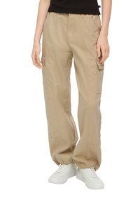 Beige cargobroek van zachte stof, met zijzakken, elastische boorden en een ontspannen pasvorm. Gedirigeerd met witte sneakers.