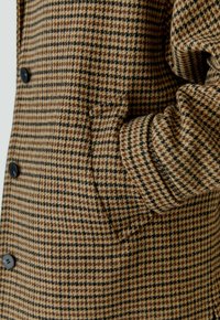 Braun und schwarz kariertes Blazer mit strukturiertem Stoff, ausgestattet mit schwarzen Knöpfen und einer Seitentasche an der Hüfte.