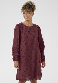Burgunderfarbenes Kleid mit langen Ärmeln, floralem Stickerei und gewelltem Saum. Weicher, transparenter Stoff mit rundem Ausschnitt und gerafftem Schulterdetail.