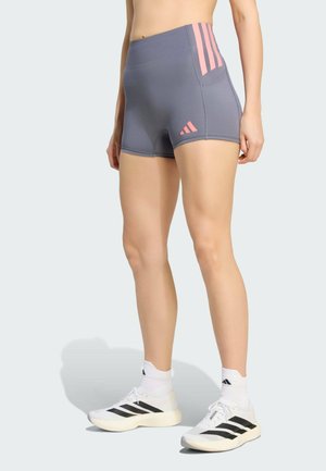 Persona che indossa pantaloncini sportivi grigi con strisce rosa e logo, calzini bianchi e scarpe da corsa bianche con strisce nere.