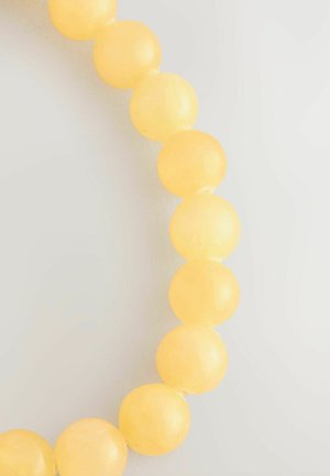  Runde perler i lys gul, halvtransparent materiale, glat overflade arrangeret i en buet linje, der fremhæver deres ensartede form og farve.