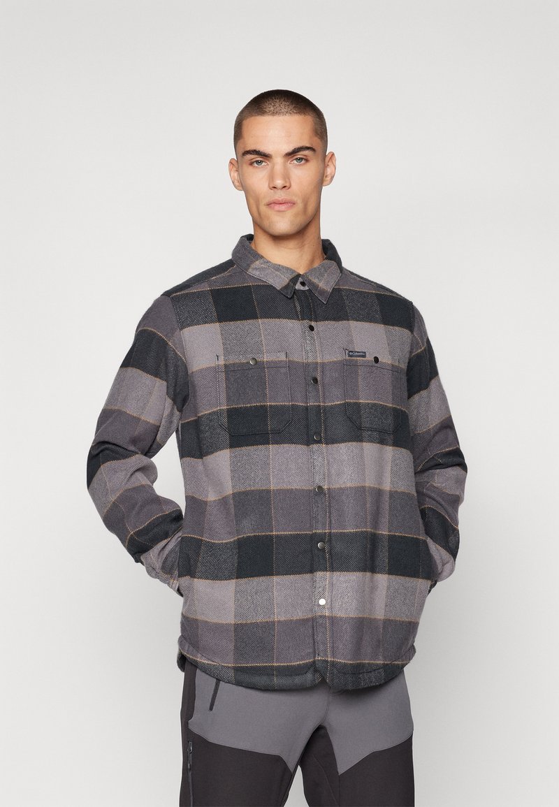 Grå og svart rutete skjorte laget av flanell, med en knapplukking foran, to brystlommer og klassisk krage-design.