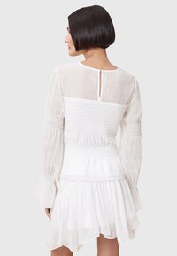 White dress featuring a smocked bodice, long sheer sleeves, and layered ruffles at the skirt, with a keyhole back detail.