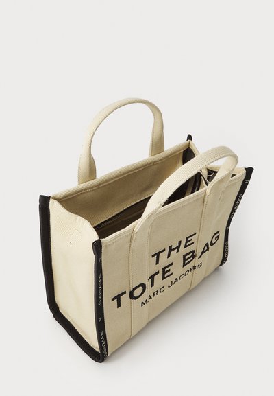 Canvas tote-väska i beige med svarta detaljer. Har dubbla handtag, ett zippered inre och fet textlogotyp på framsidan.