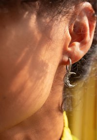 Boucle d'oreille en argent en forme de croissant de lune avec des détails complexes. Suspendue à une boucle, mettant en valeur un métal poli et une surface texturée. Vue en gros plan.