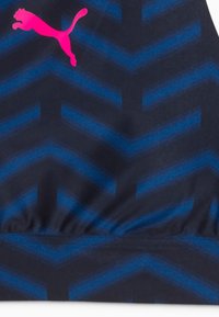 Tejido atlético azul marino con patrón de espiga. Logo de Puma en rosa brillante, exhibido de manera prominente. Textura suave con detalle de cintura fruncida.