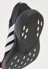 Scarpa sportiva bianca e nera con suola in gomma che presenta inserti bianchi per la presa e tre strisce bianche sul lato.