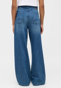 Dżinsy w szerokim kroju w średnim niebieskim odcieniu, z dwiema tylnymi kieszeniami i subtelnym detalem ściegowym w kształcie góry oraz standardowym paskiem.