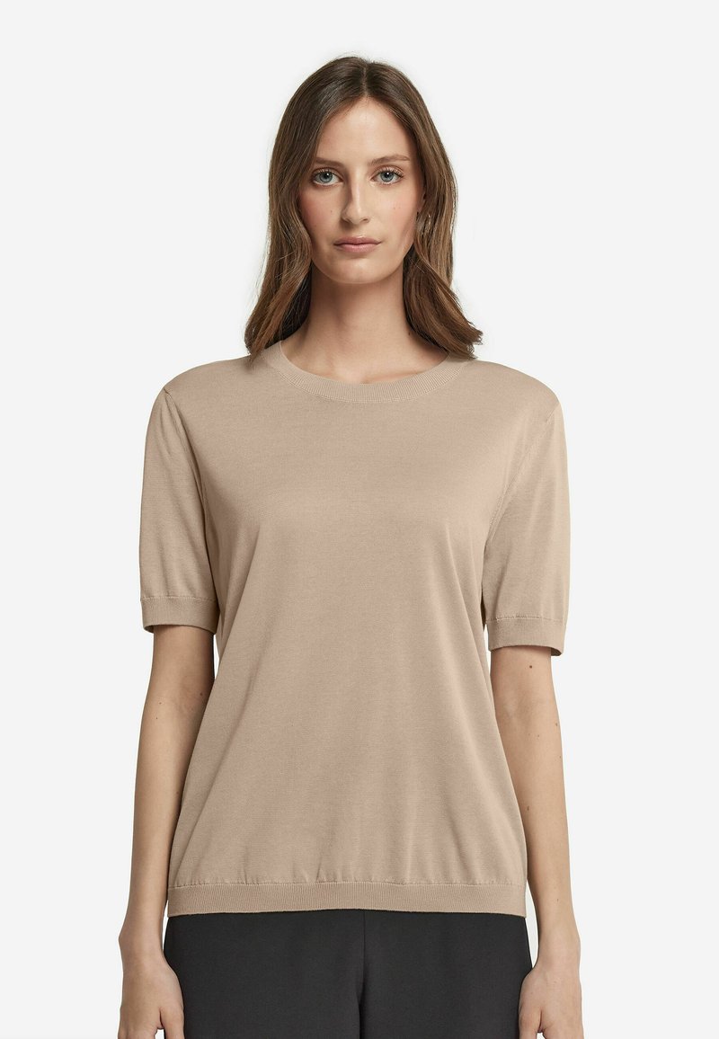 Beige strik bluse med korte ærmer, rund halsudskæring og ribbet kant. Blød tekstur med en afslappet pasform, stylet over mørke bukser.
