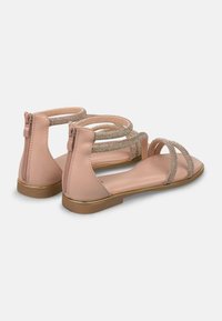 Sandalias planas rosas con múltiples tiras, adornadas con acentos metálicos y cierre de cremallera trasera. Textura suave con un tacón bajo.