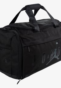 Bolsa de deporte negra con una textura suave, que presenta un prominente logo negro de "JORDAN" y una correa ajustable, con un cierre superior con cremallera.
