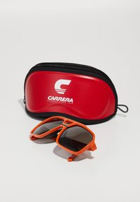 Carrera prillid, millel on oranž plastikraam ja tume lääts, asuvad punase ja musta tõmblukuga kotiga, millel on Carrera logo.