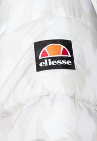 Pannello con logo Ellesse su tessuto imbottito bianco e grigio chiaro a camouflage, probabilmente parte di una giacca o di un indumento esterno.