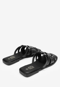 Sandales plates noires avec design de bride tissée, bout carré et finition mate lisse. Elles disposent d'une semelle flexible et d'un détail de logo subtil sur la semelle intérieure.