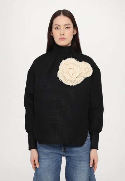 Pull en maille noir texturé avec col haut ; présente un accent tressé en crème, diagonal, sur l'épaule avant.