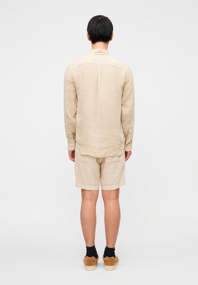 Μπεζ λινό πουκάμισο με μακριά μανίκια και χαλαρή εφαρμογή, συνδυασμένο με ταιριαστό σορτς. Η εμφάνιση διαθέτει ελαφριά υφή και απλό σχέδιο.