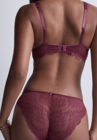 Vue dorsale d'une personne portant un ensemble coordonné de soutien-gorge et culottes en dentelle bordeaux, mettant en avant des motifs floraux en dentelle complexes et des bretelles ajustables.