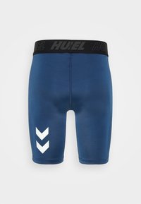 Mörkblå sportshorts med svart midjeband som har "HUEL"-logotypen. Vit chevronmönster på nedre vänstra sidan. Slät, elastisk tyg.