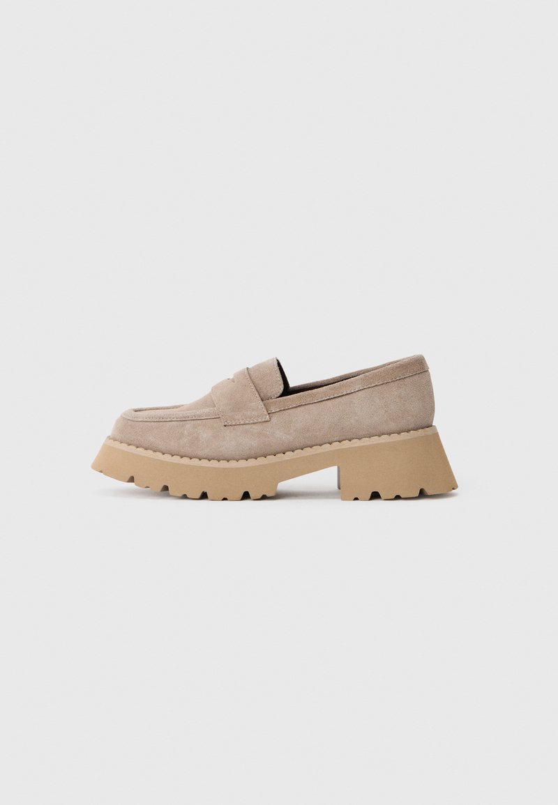 Beige Wildleder-Slipper mit dicker, gerippter Sohle. Verfügt über eine gestickte Schürze, ein breites Band an der Vorderseite und eine abgerundete Zehenpartie.