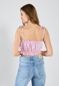 Crop top floral rose avec ourlet froncé et bretelles réglables. Porté avec un jean taille haute bleu clair, mettant en valeur un design décontracté.